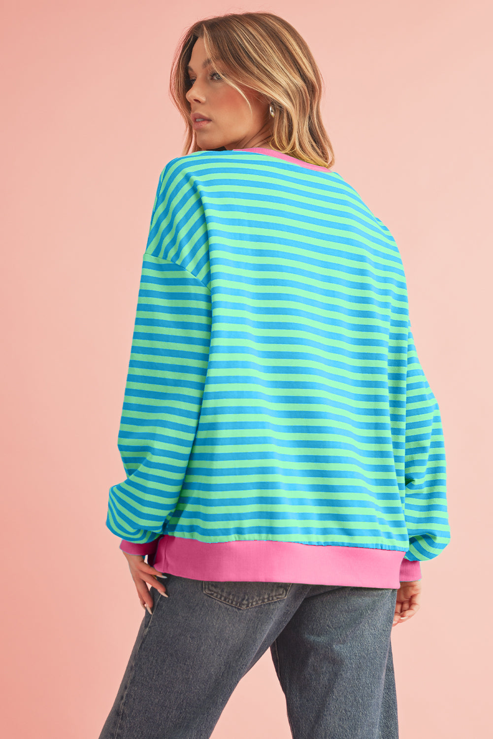 Person wearing a colorful striped sweater with pink trim on a pink background