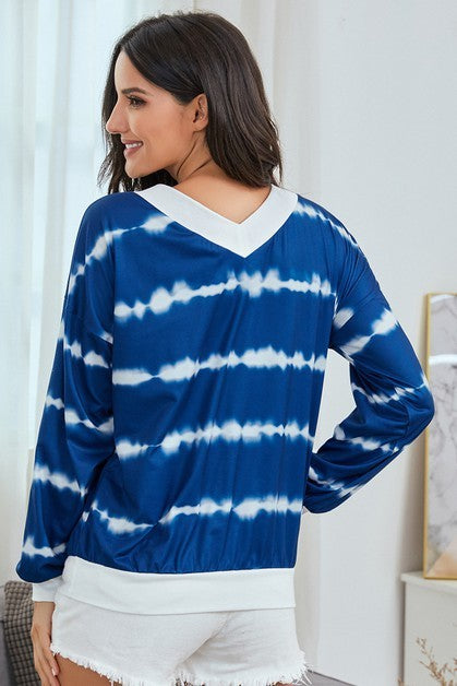 Woman wearing a blue and white tie-dye long-sleeve top in a room.
