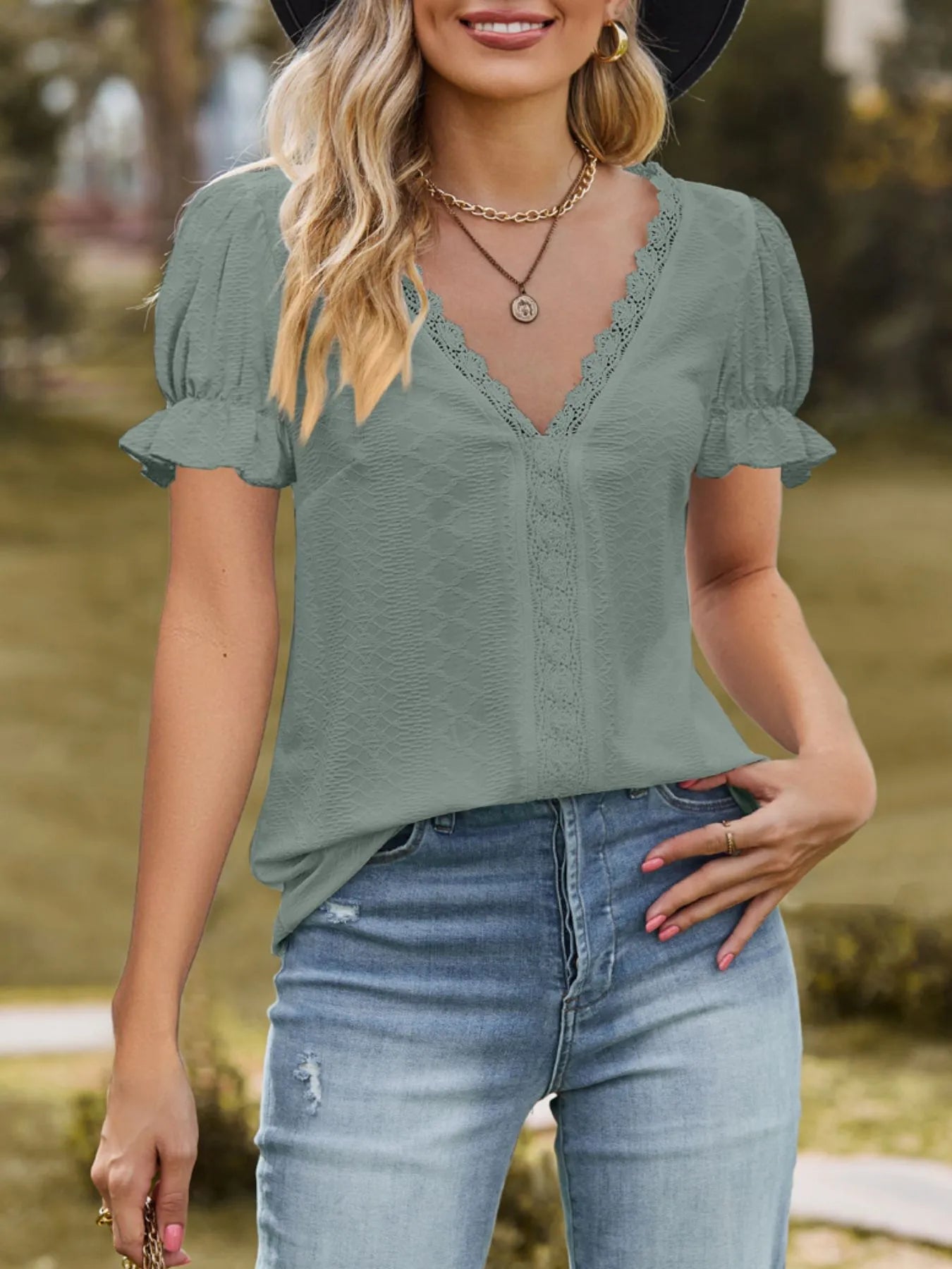 Woman wearing a green blouse with lace details and blue jeans outdoors.