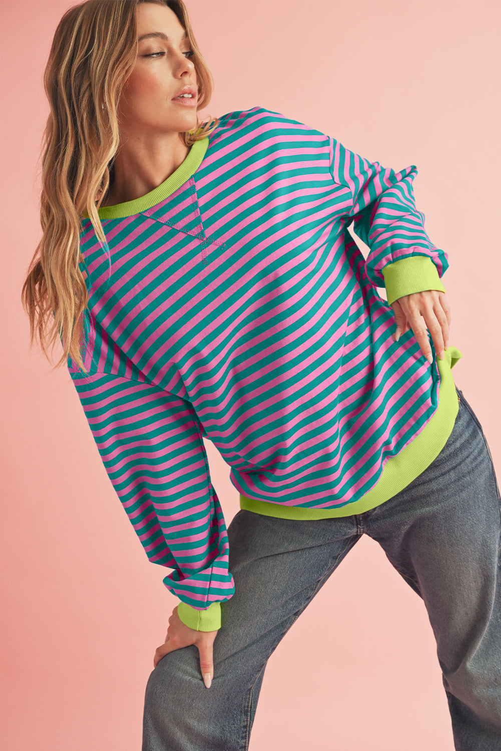 Woman wearing a striped hoodie with green and pink horizontal stripes on a pink background