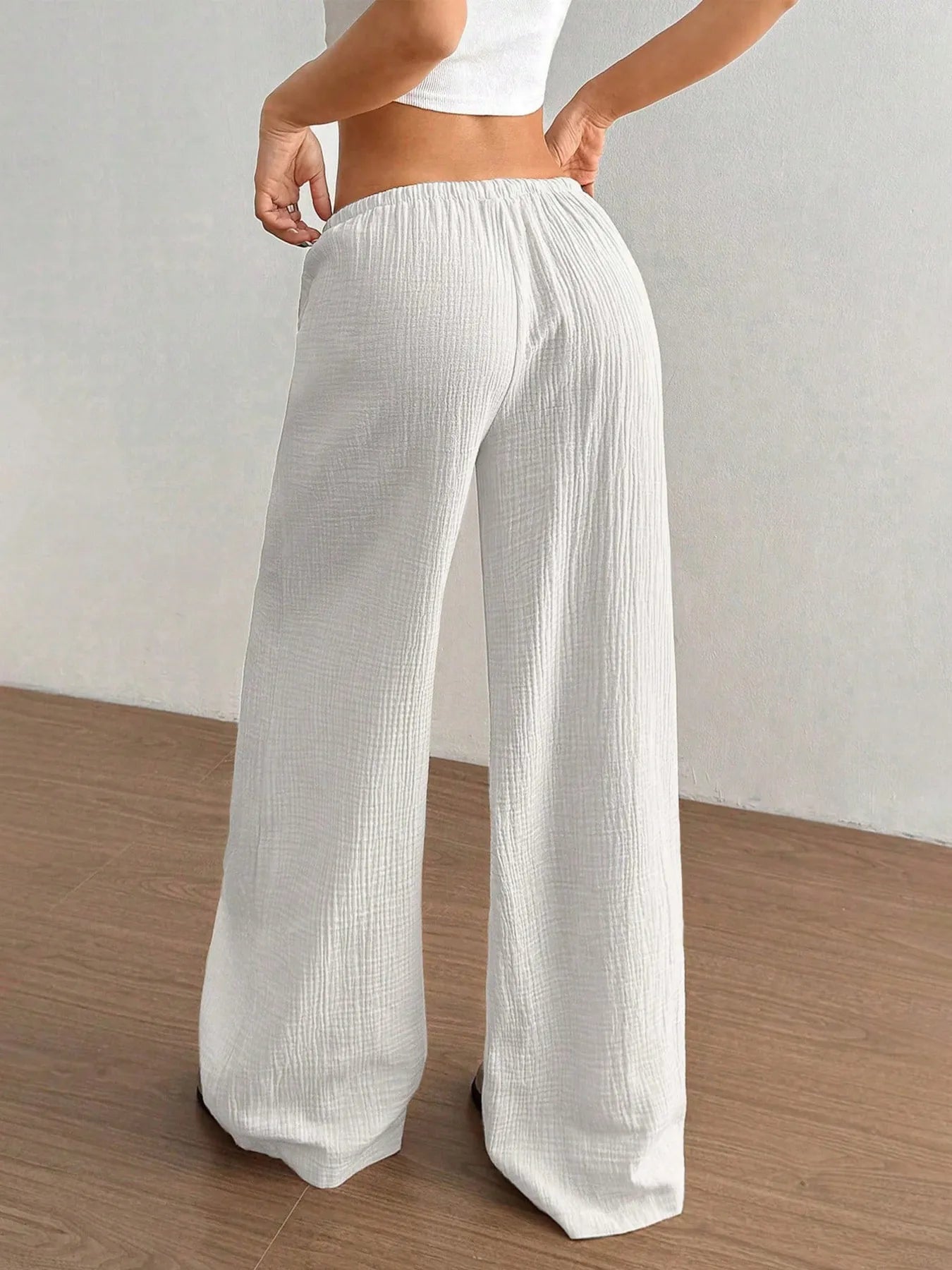 White wide-leg pants worn by a person on a wooden floor with a white wall background