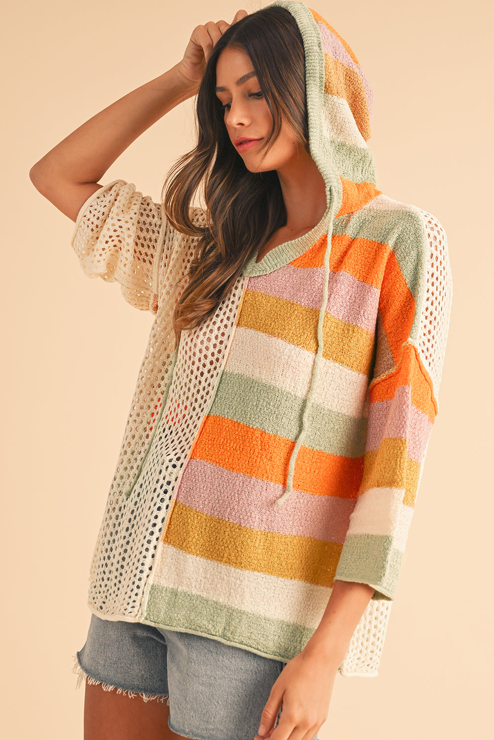 Woman wearing a colorful striped sweater with a beige mesh overlay on a beige background