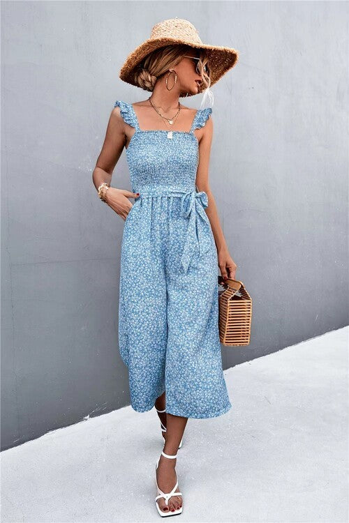 Woman wearing a light blue dress with wide-leg pants and a straw hat against a gray wall.