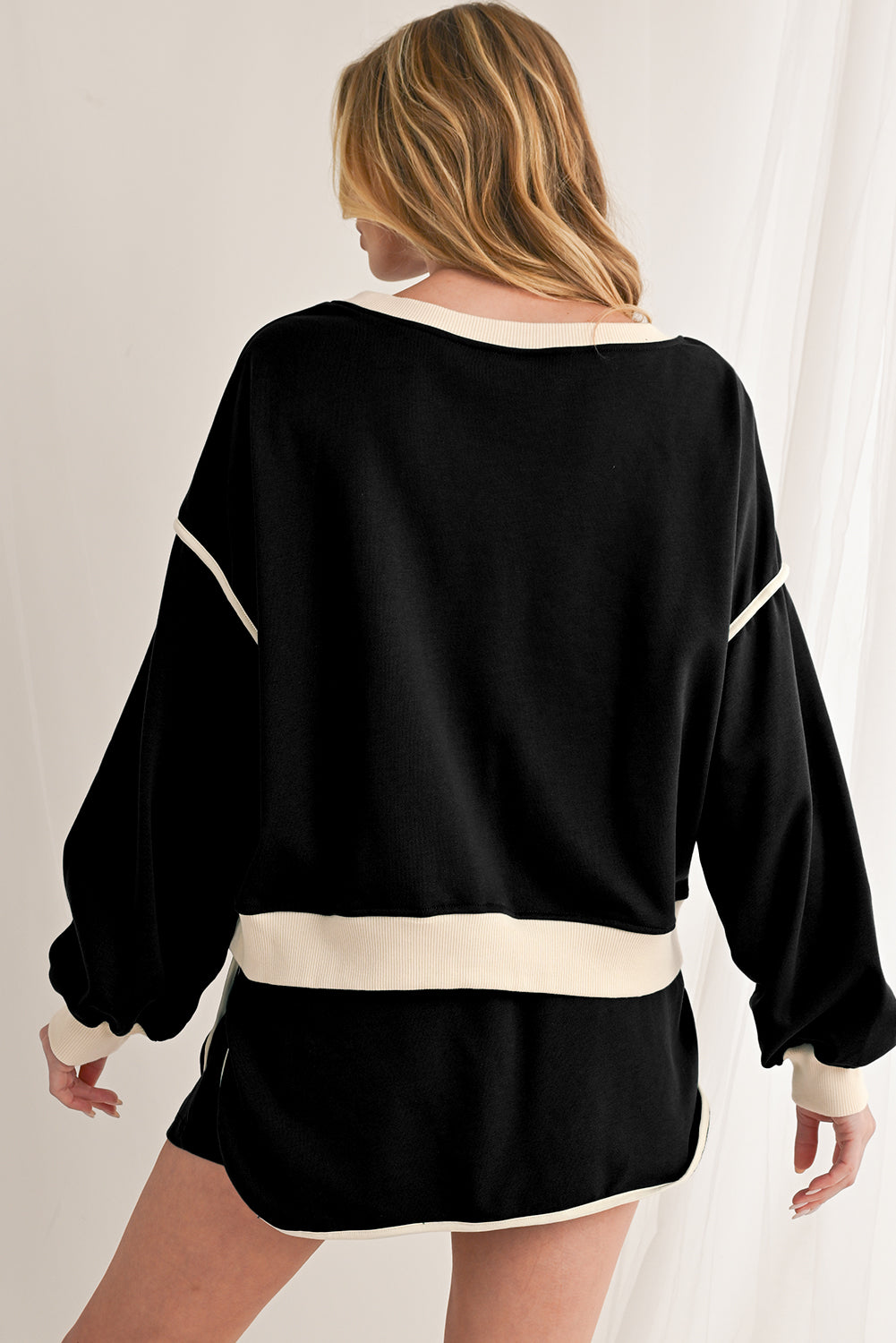 Person wearing a black sweater with white trim on a plain background