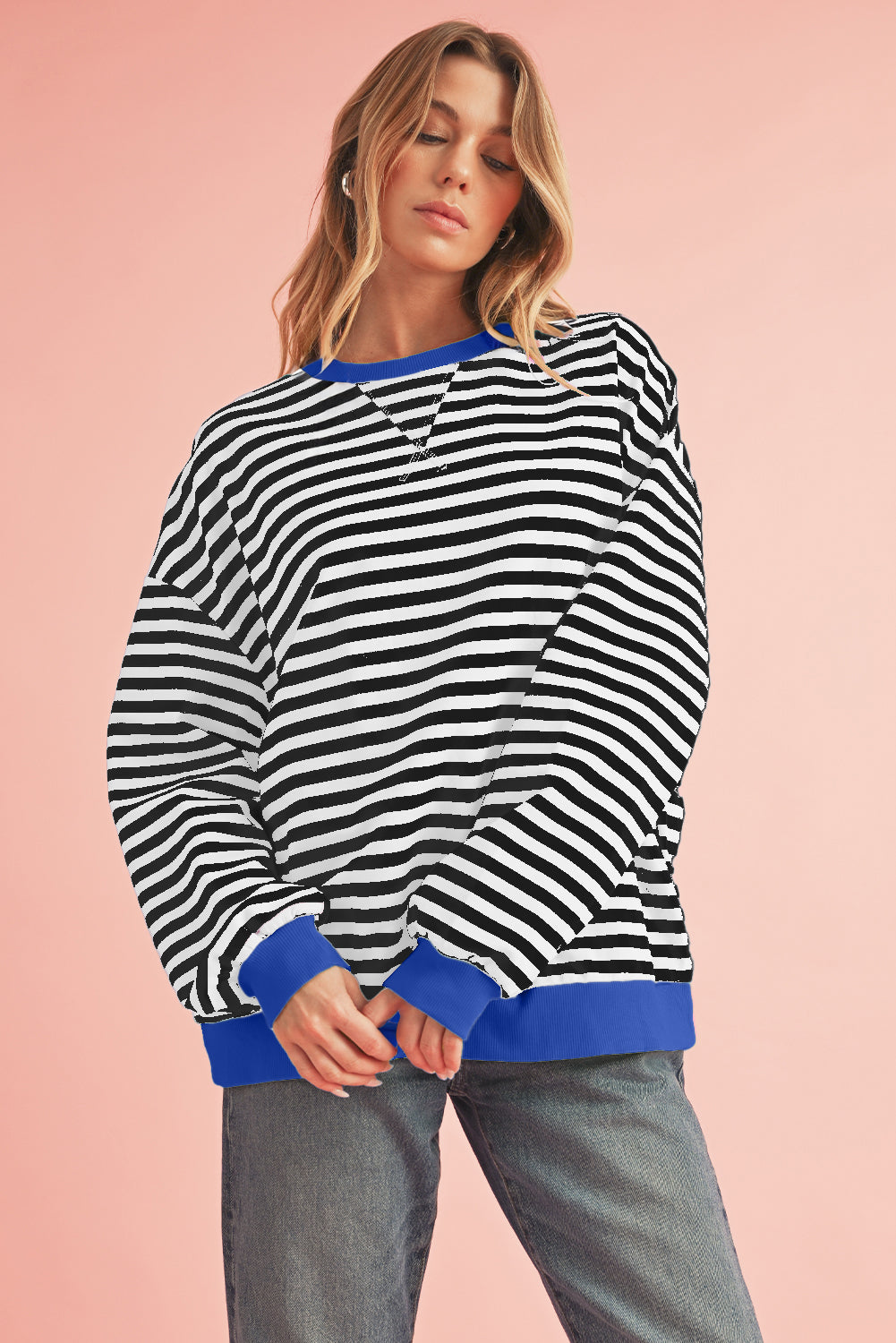 Woman wearing a black and white striped sweater with blue trim on a pink background