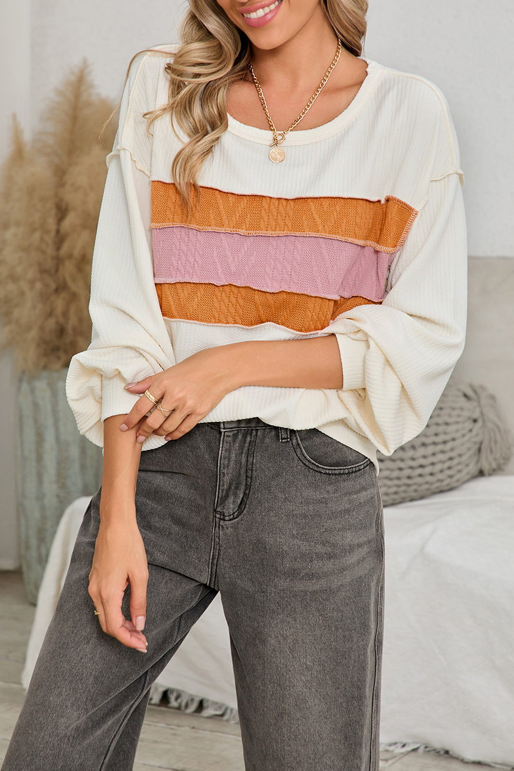 Woman wearing a white long-sleeve top with colorful stripes and gray jeans indoors.