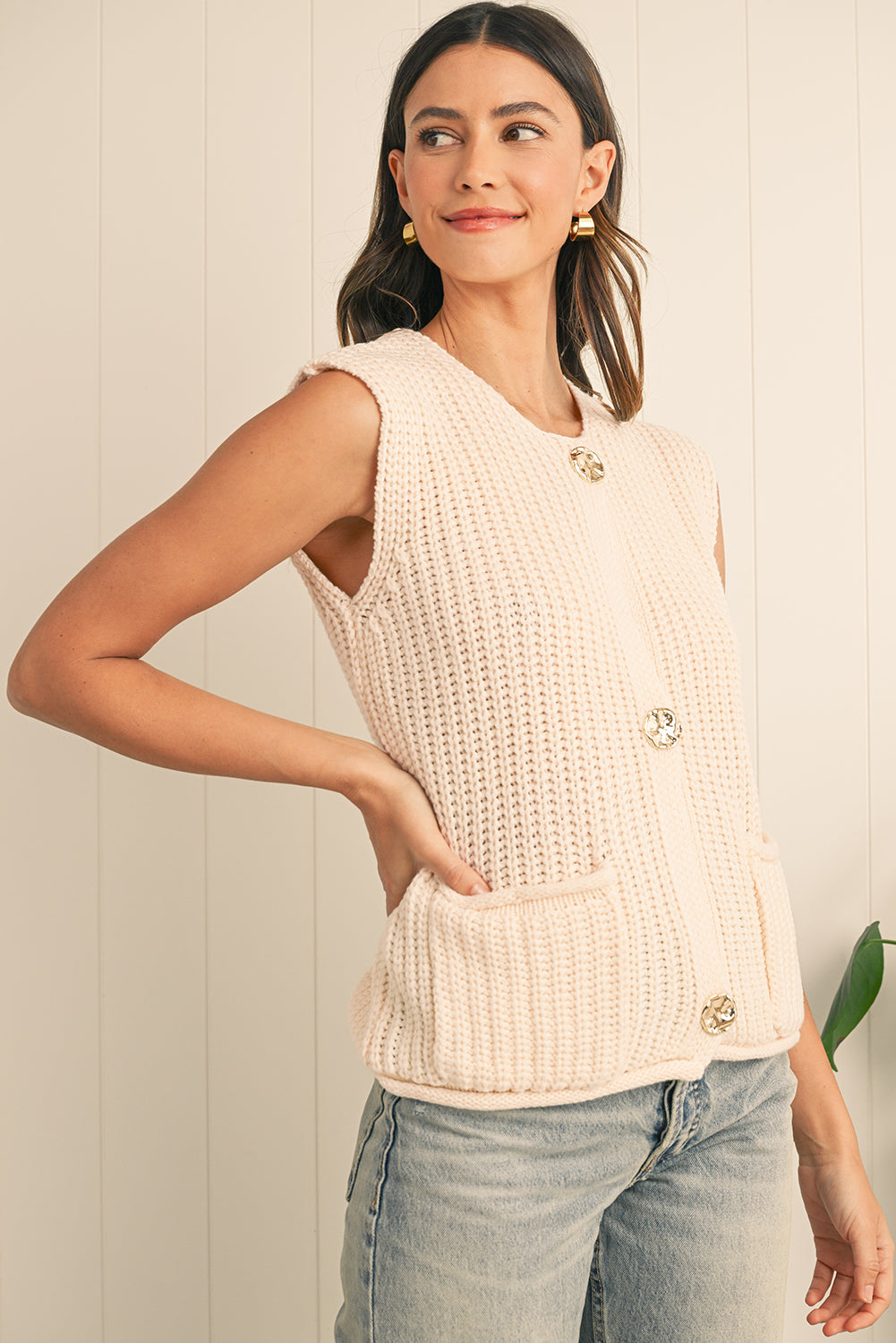 Woman wearing a beige knitted sleeveless top with buttons against a light background