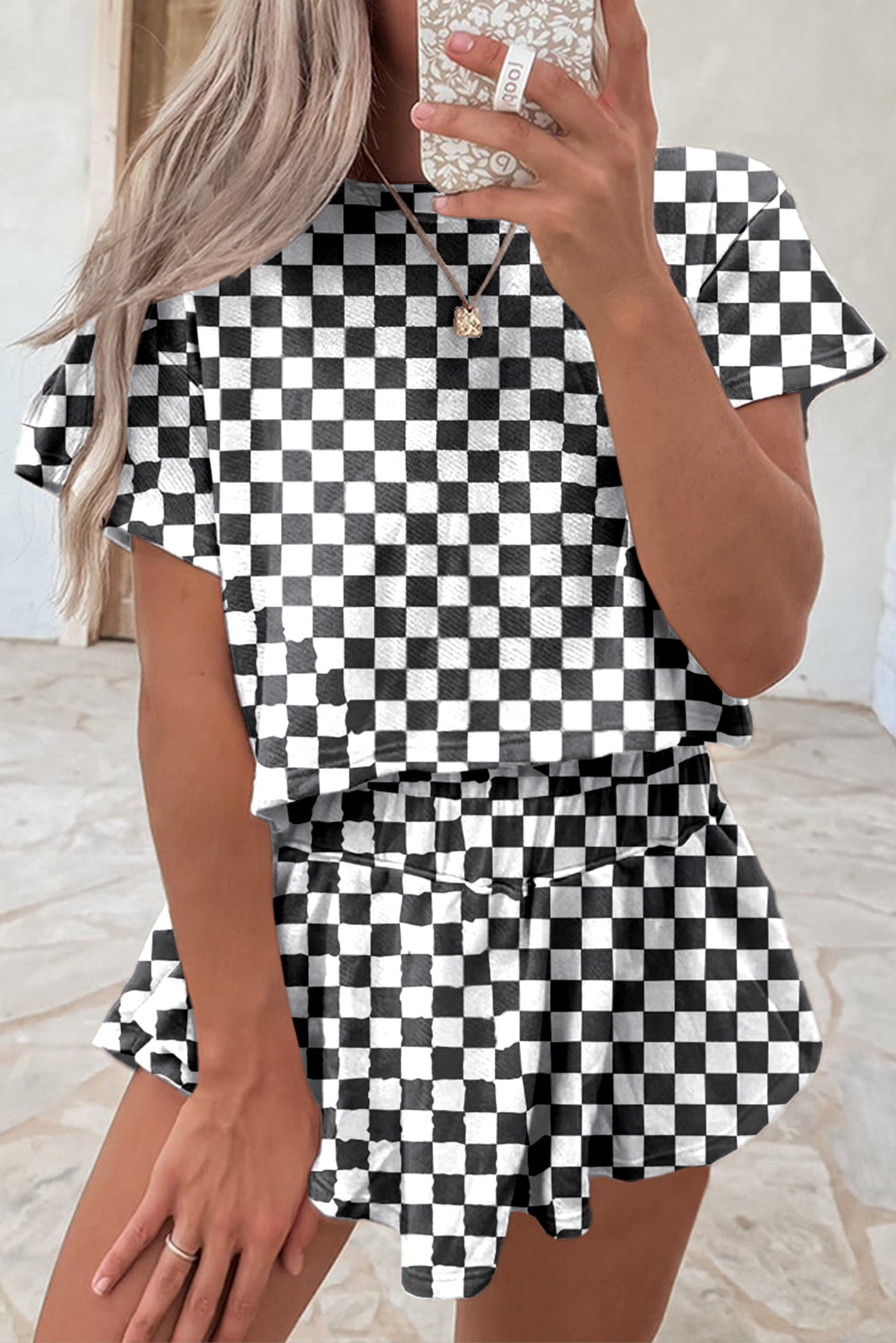 Person wearing a black and white checkered outfit taking a mirror selfie.