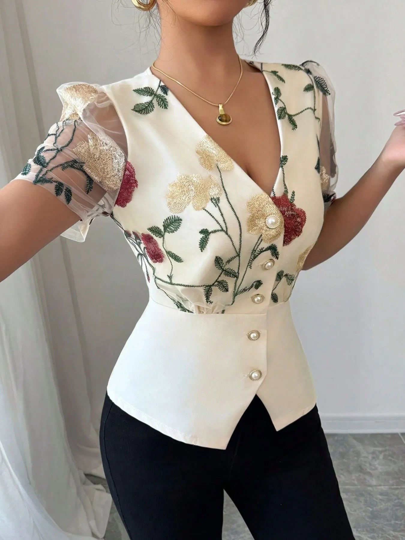 Woman wearing a floral embroidered blouse with sheer sleeves against a neutral background