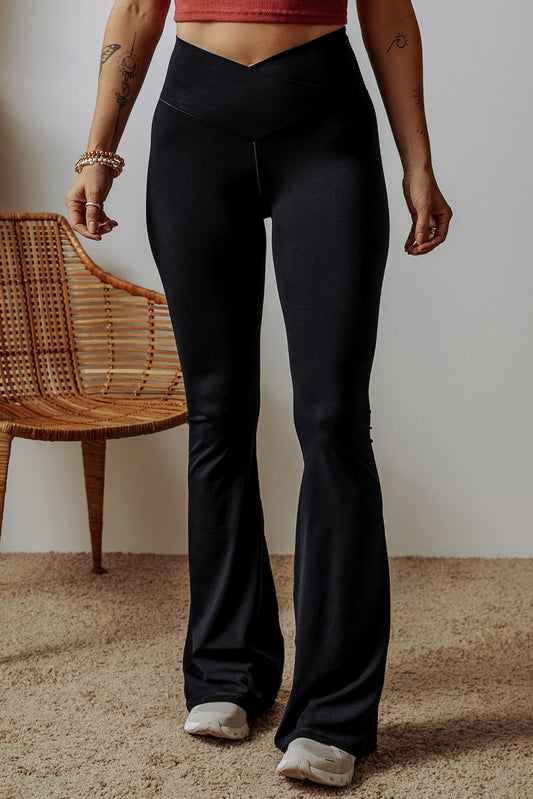 Person wearing black flared pants standing in a room with a wooden chair and beige carpet.