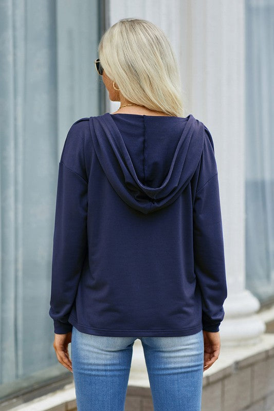 Person wearing a navy blue hoodie and light blue jeans standing against a neutral background