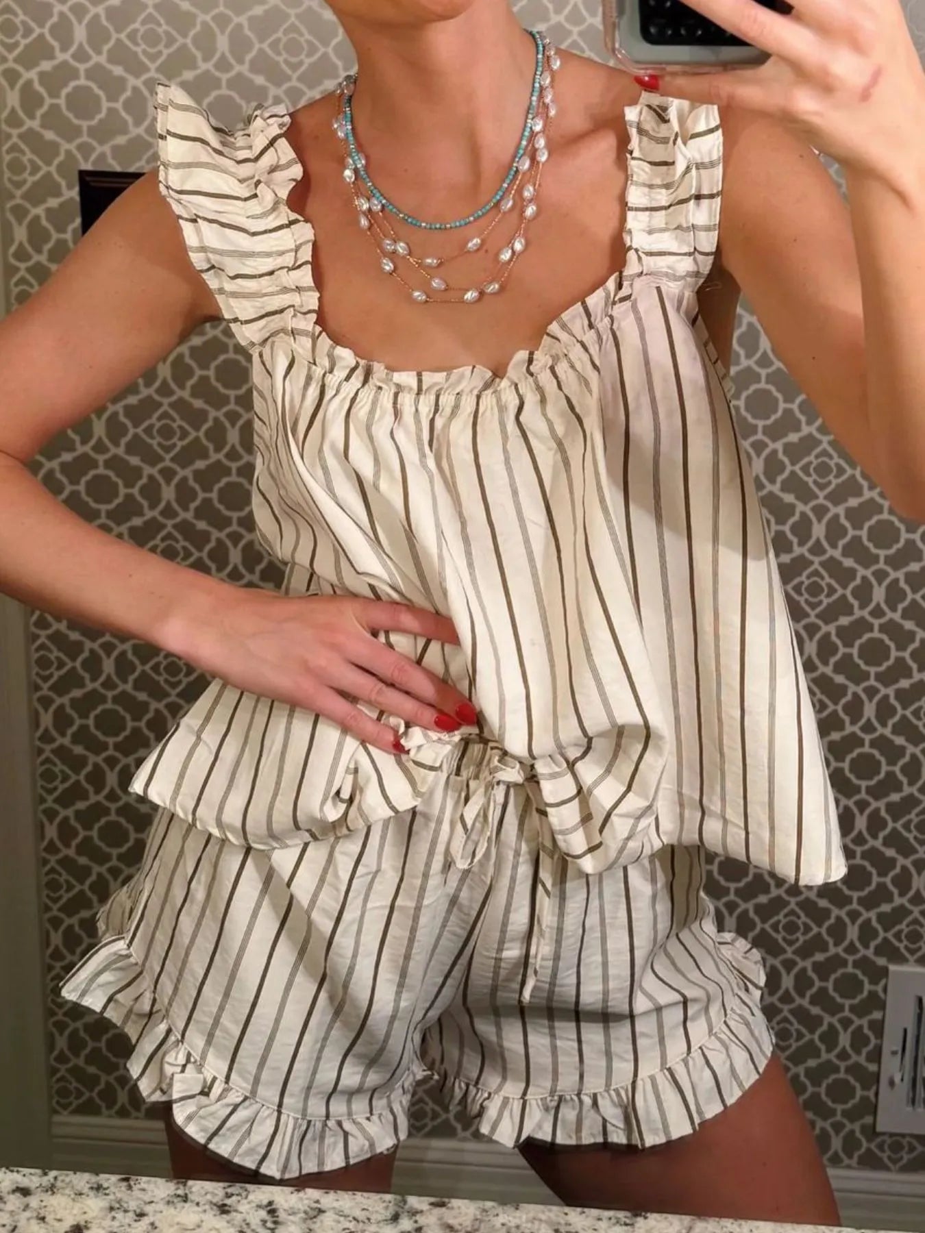 Person wearing a striped romper with ruffled details in front of a patterned wall.