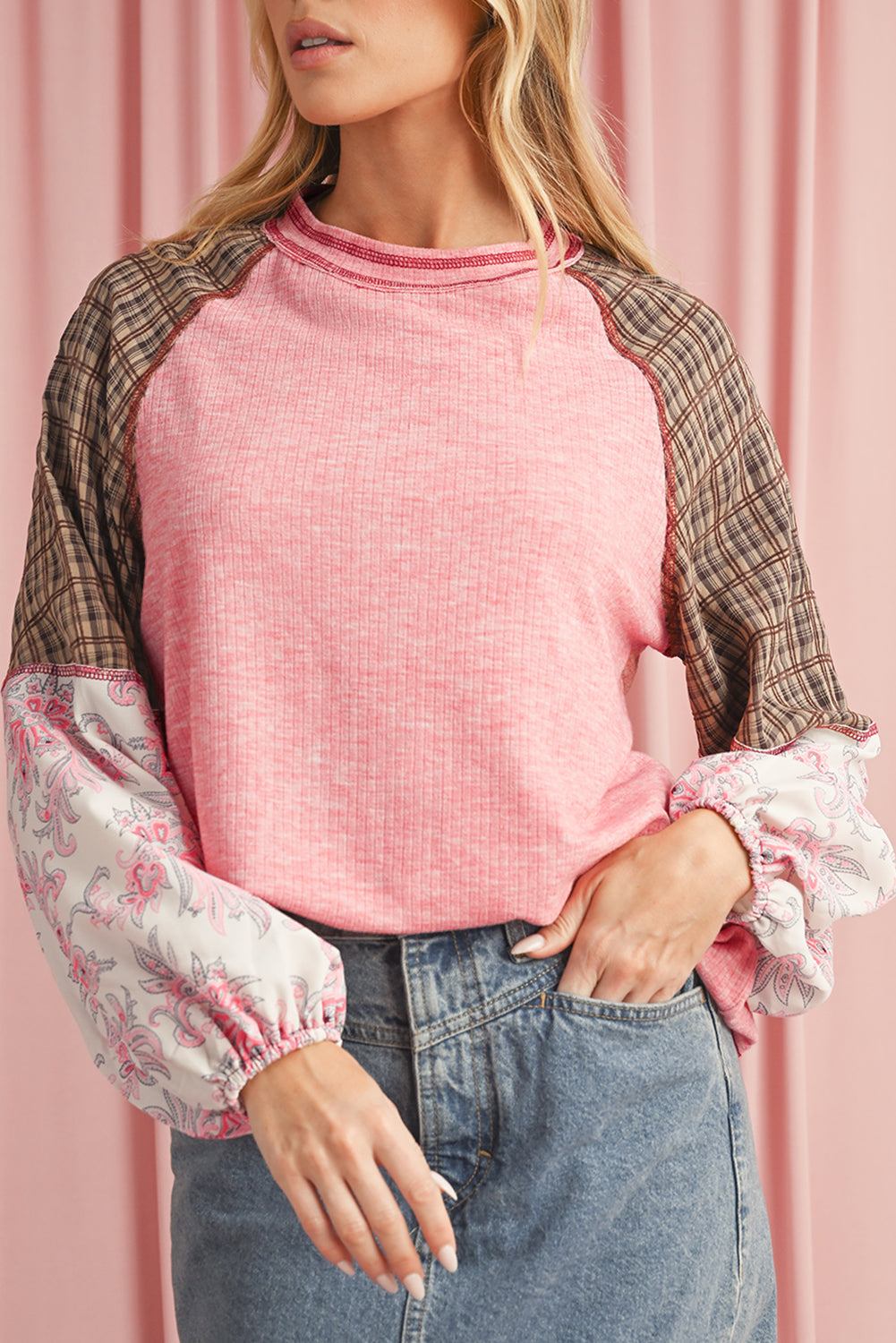 Woman wearing a pink top with plaid and floral sleeves against a pink background