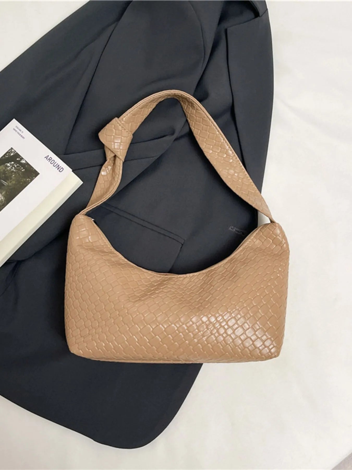 Beige handbag on a dark gray blazer with a magazine underneath