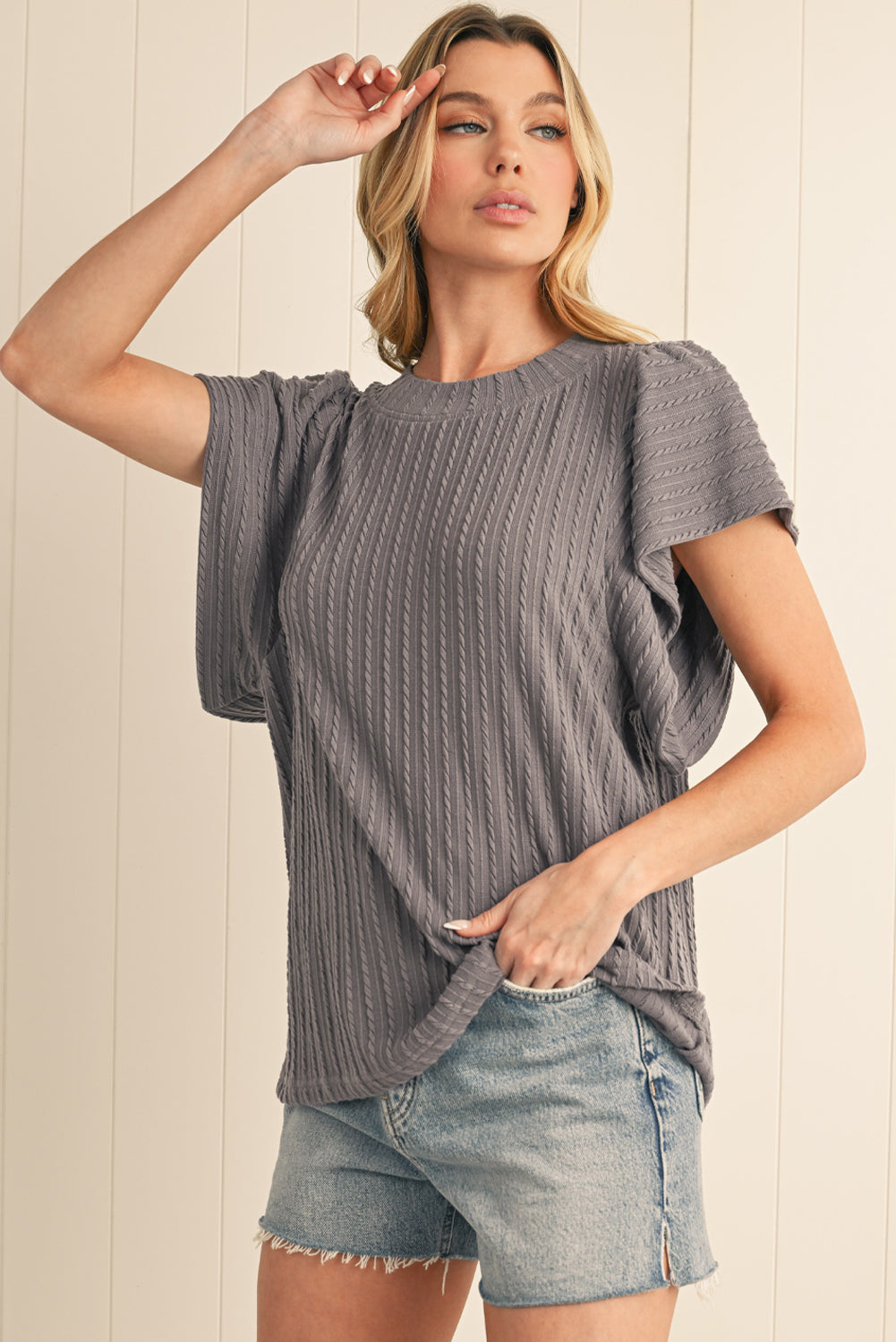 Woman wearing a gray ribbed top and denim shorts against a beige wall.