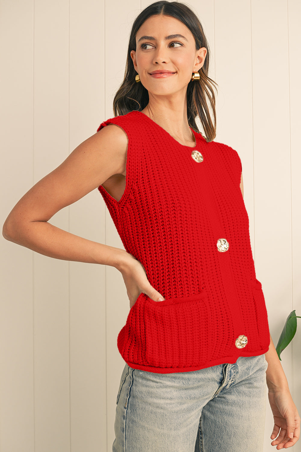 Woman wearing a red knitted sleeveless top with buttons against a light background