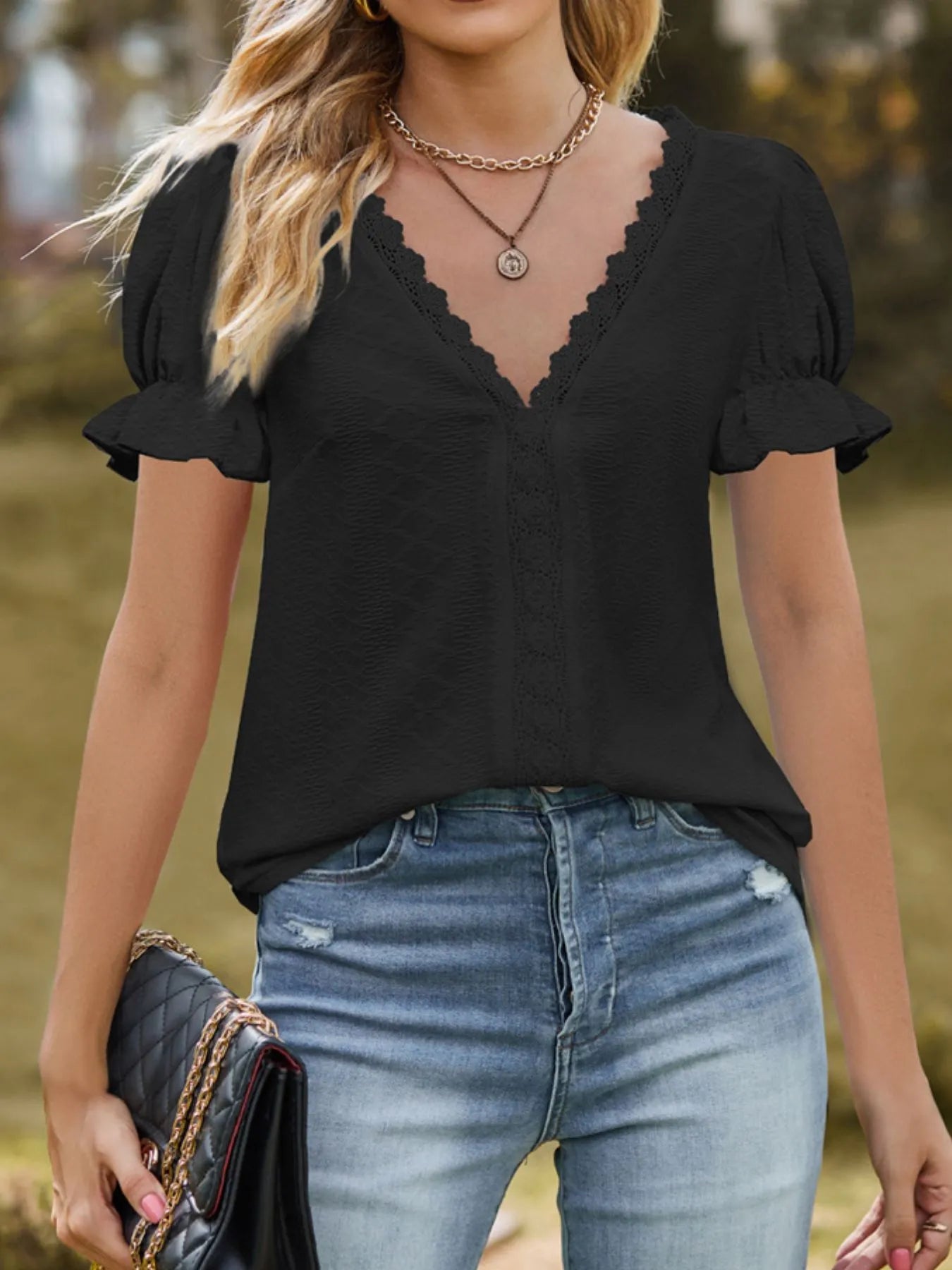 Woman wearing a black top with lace detail and blue jeans, holding a black clutch.