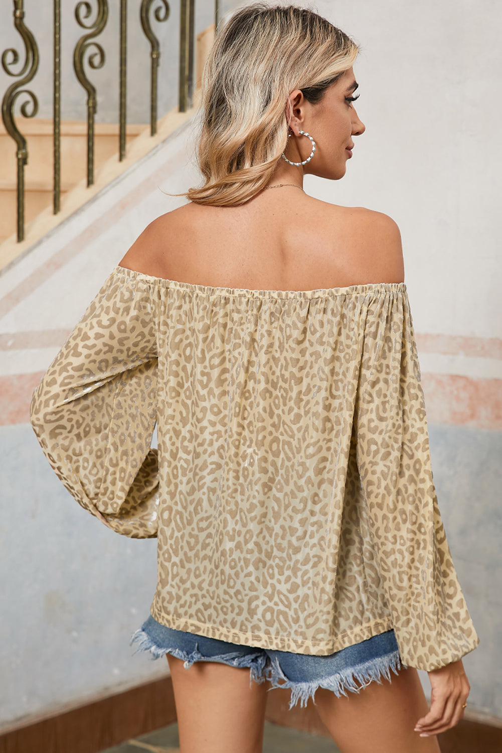 Woman wearing a leopard print off-shoulder top and denim shorts, standing on a staircase.