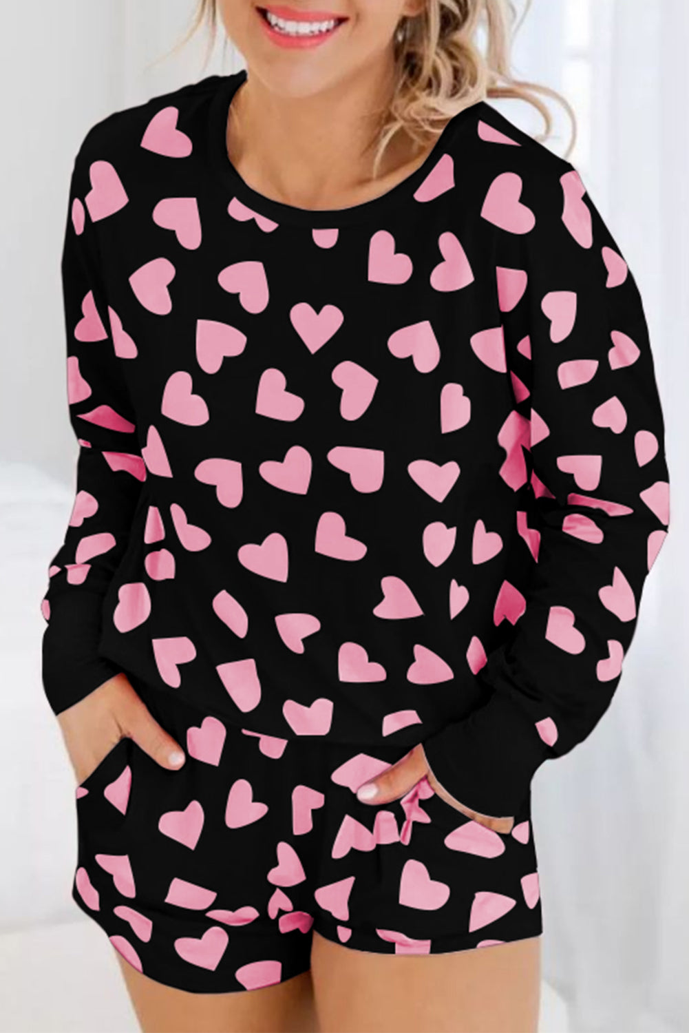 Black pajama set with pink heart patterns worn by a person.
