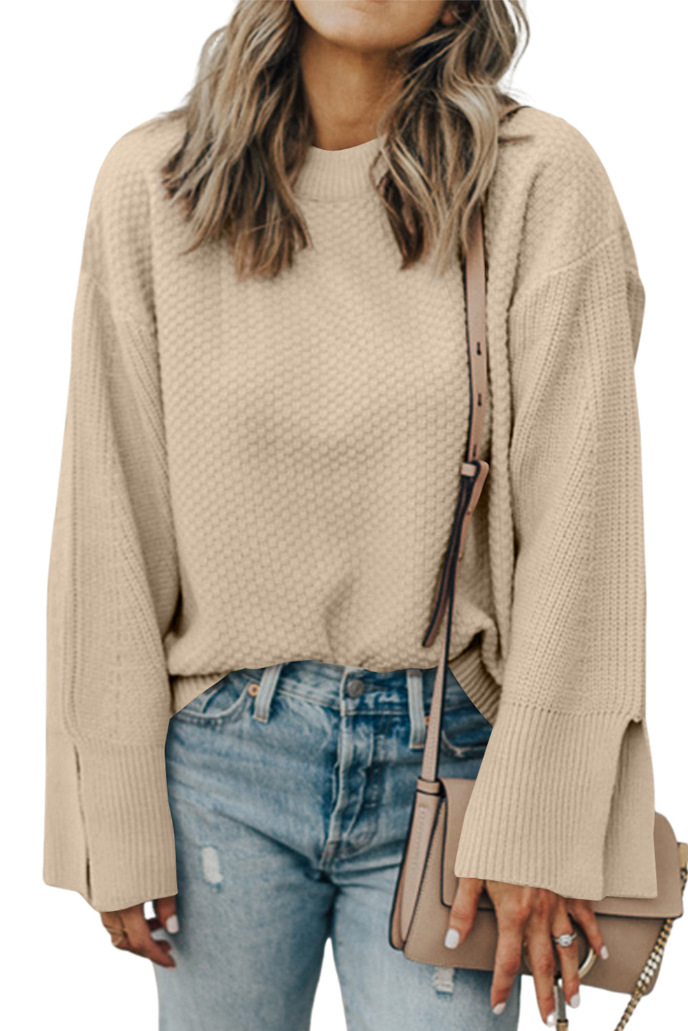 Person wearing a beige sweater and blue jeans, holding a beige handbag.