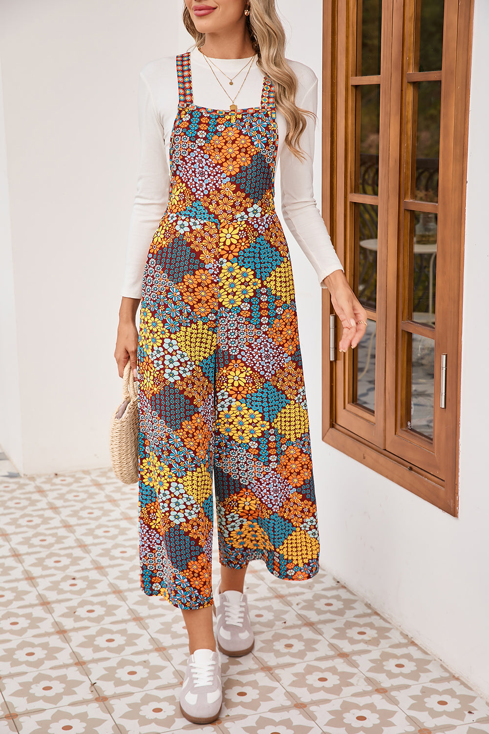 Woman wearing a colorful floral dress with a white shirt underneath, standing in a room with wooden doors.