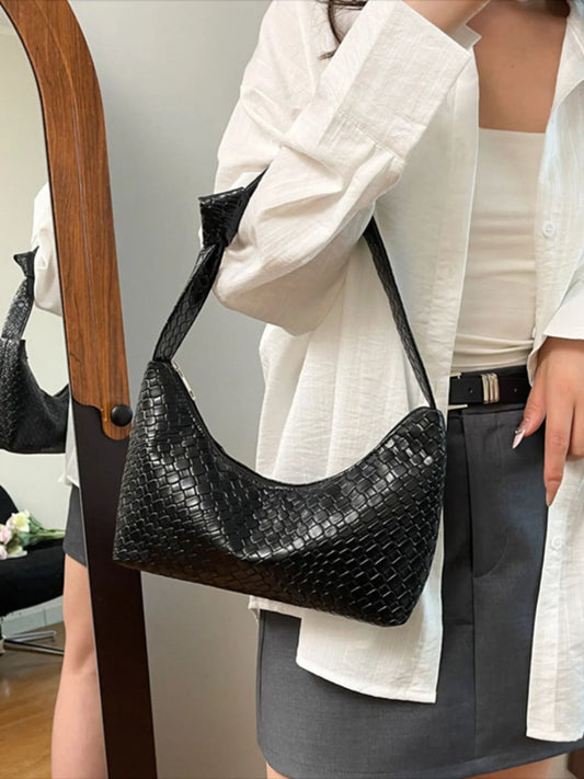 Person holding a black handbag with a textured pattern, wearing a white shirt and gray skirt.
