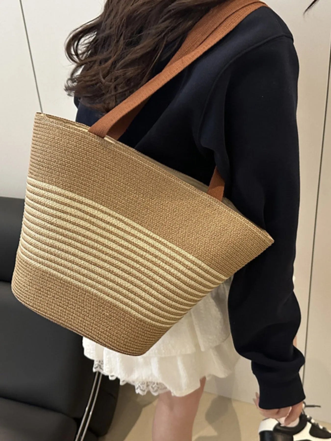 Person holding a straw handbag with a brown strap indoors.