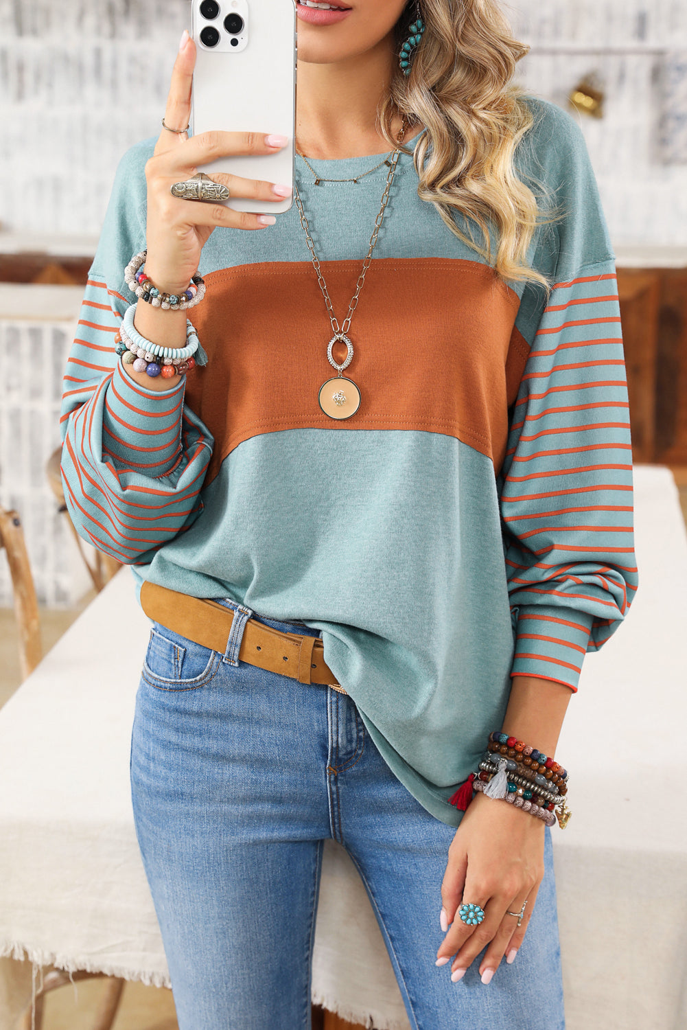 Woman wearing a colorful sweater and jeans, taking a selfie.