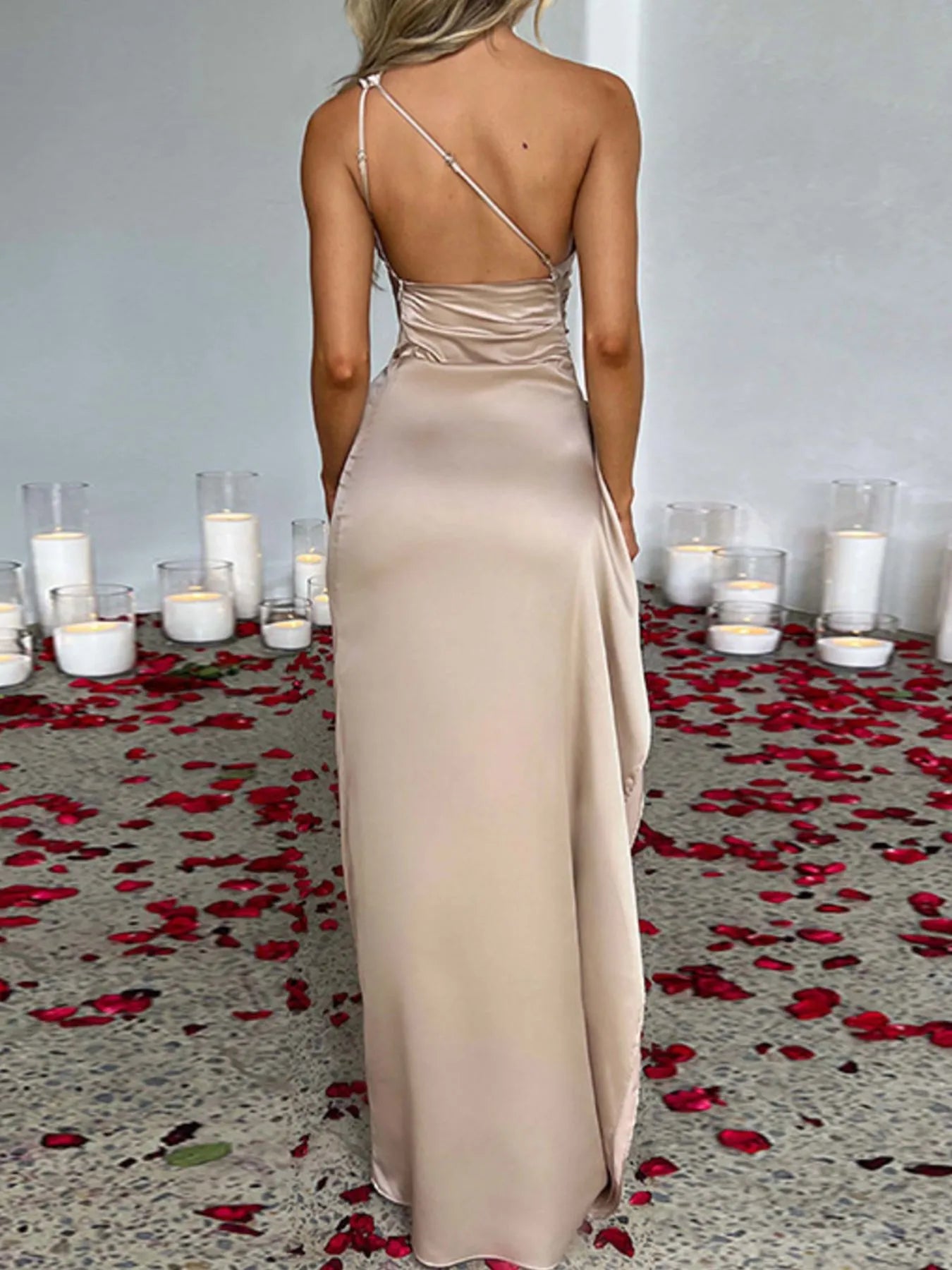 Woman in a beige evening gown standing in front of candles and rose petals on a floor.
