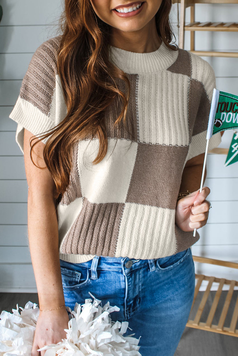 Woman wearing a checkered sweater and blue jeans holding a magazine.