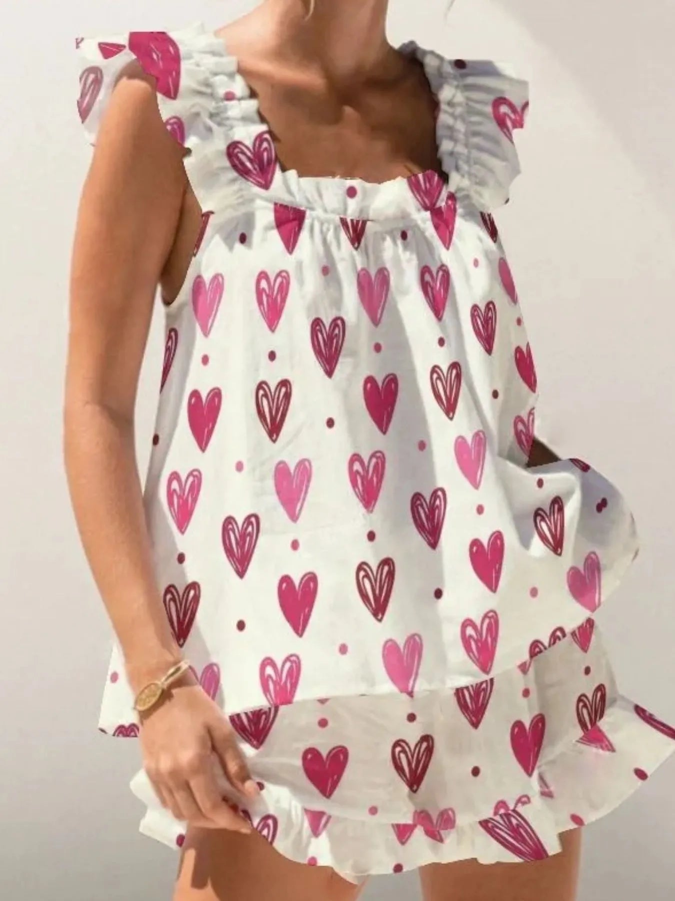 White dress with pink heart patterns worn by a person on a plain background