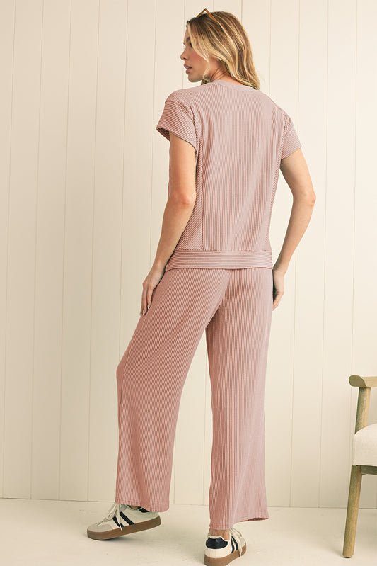 Woman wearing a pink ribbed outfit against a light wooden panel background