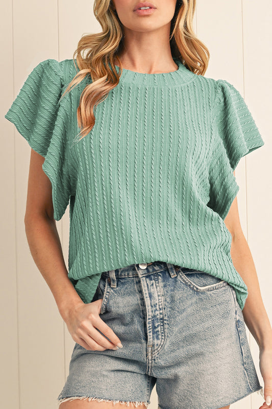 Woman wearing a green textured top and denim shorts against a neutral background