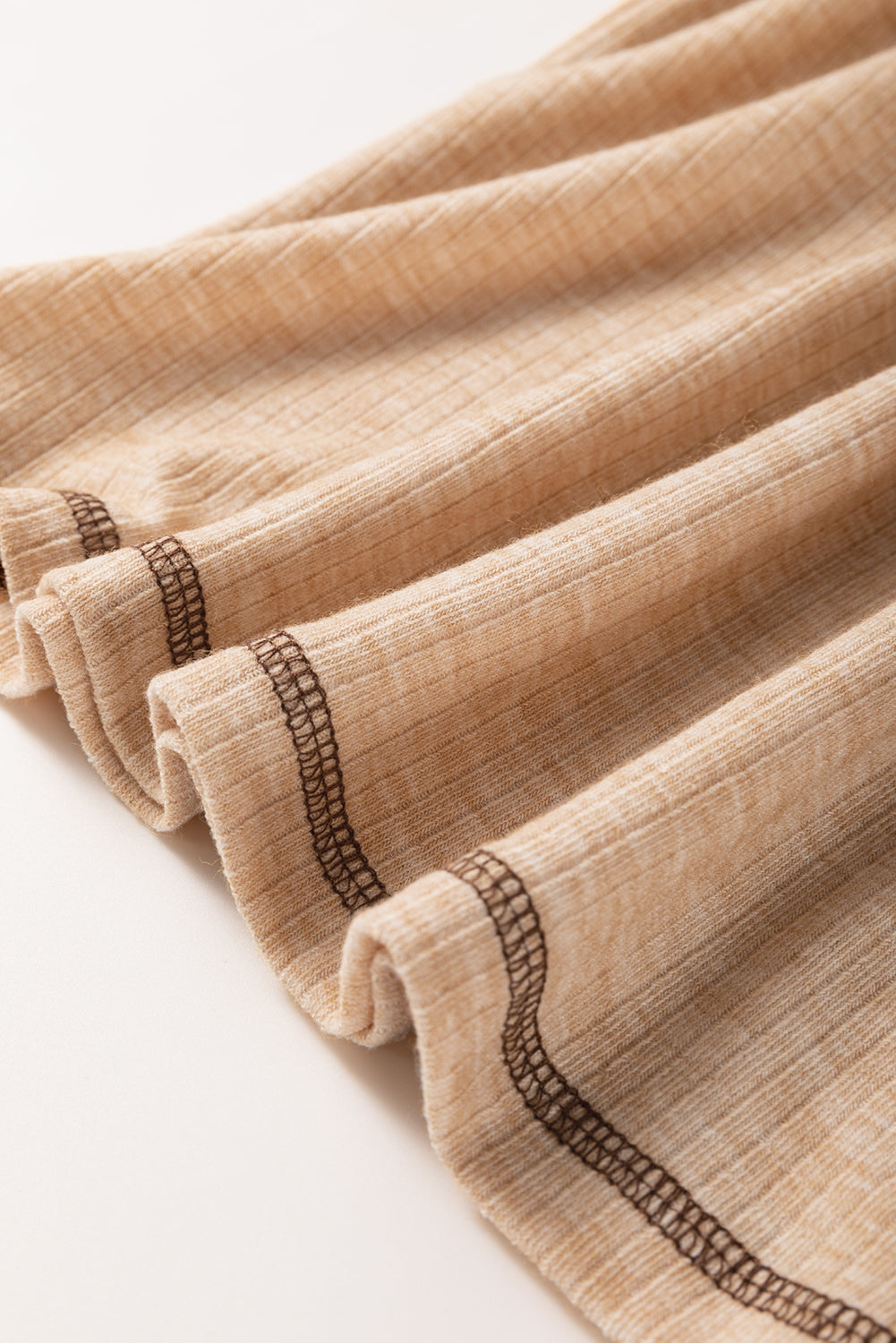 Close-up of beige fabric with brown stitching on a white background