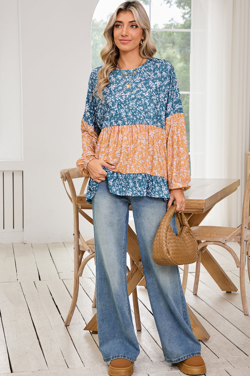 Woman wearing a patterned top and jeans standing in a room with wooden flooring and furniture.