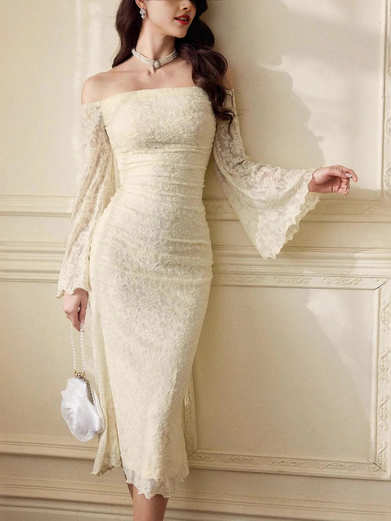 Woman wearing a white lace dress against a beige wall.