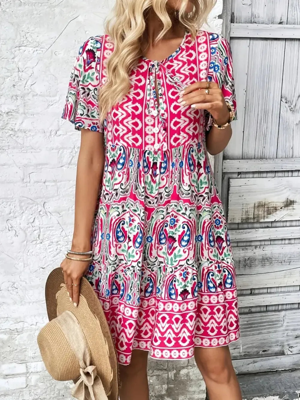 Woman wearing a colorful patterned dress against a white brick wall.