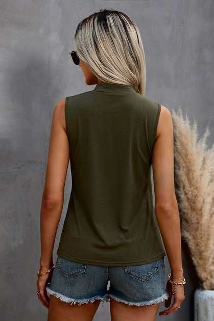 Woman wearing a green sleeveless top and denim shorts against a gray background