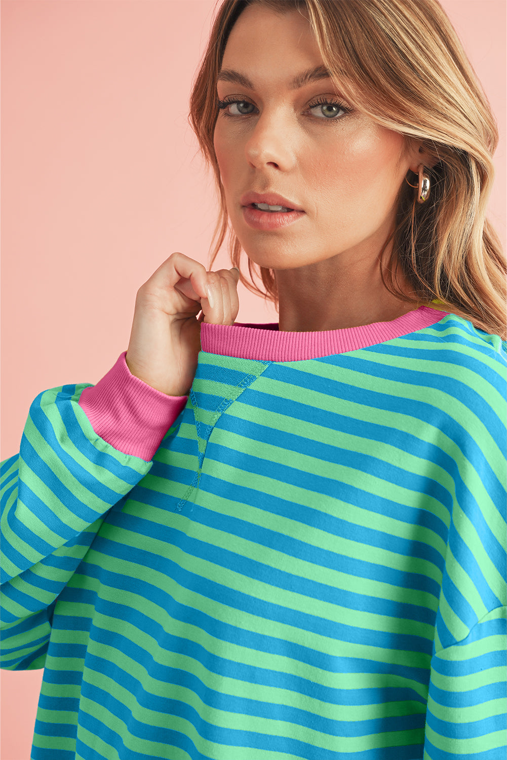 Woman wearing a green and blue striped sweater with pink trim against a pink background