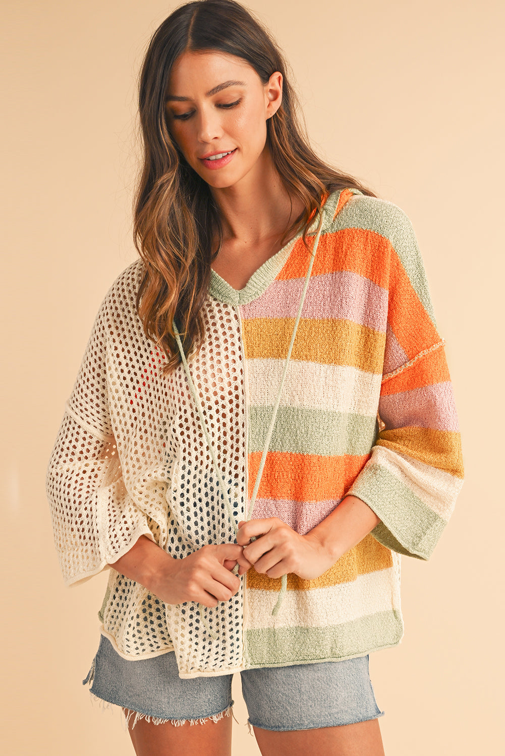 Woman wearing a colorful striped poncho over a patterned top and shorts on a beige background