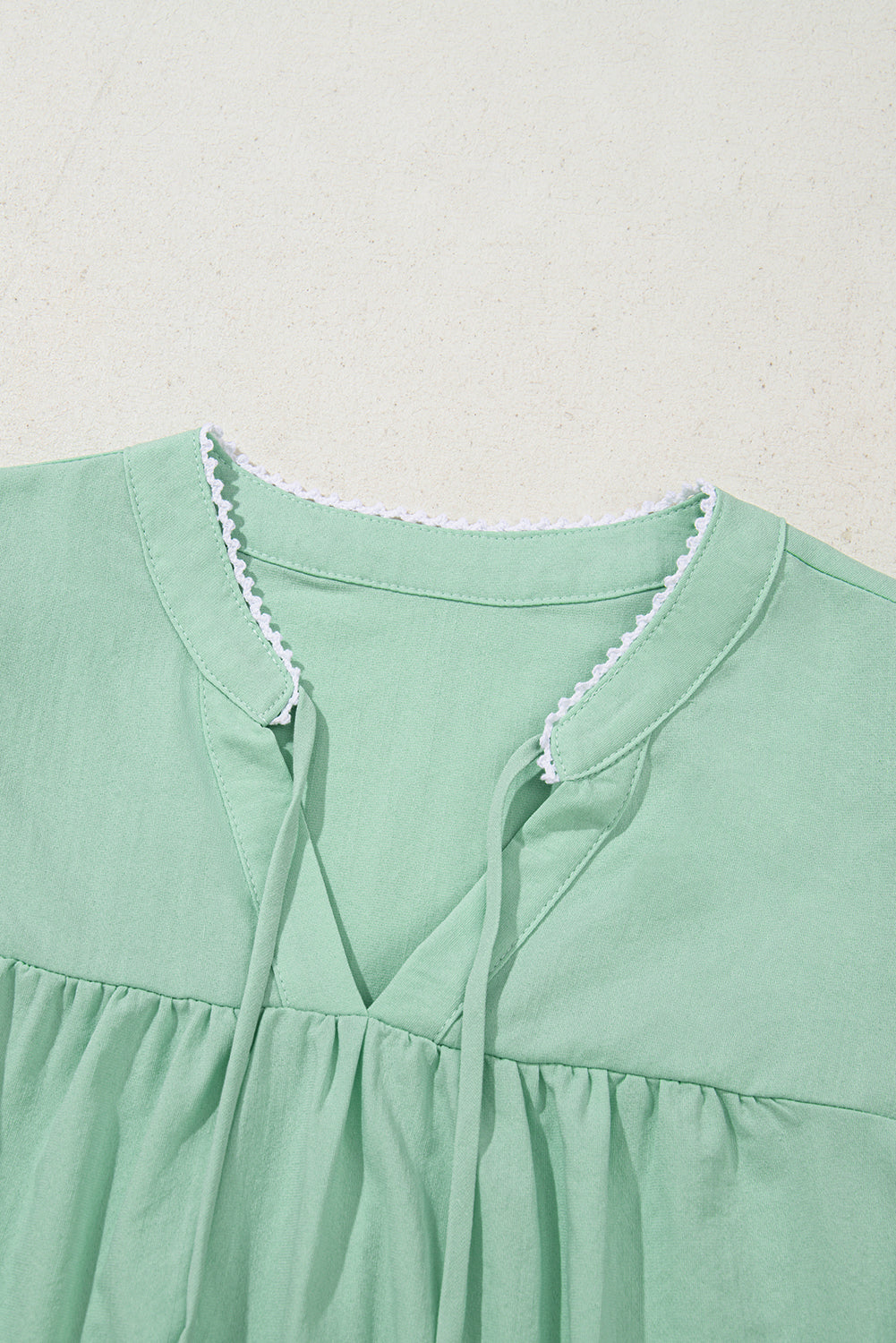 Close-up of a green dress with lace trim on a light gray background