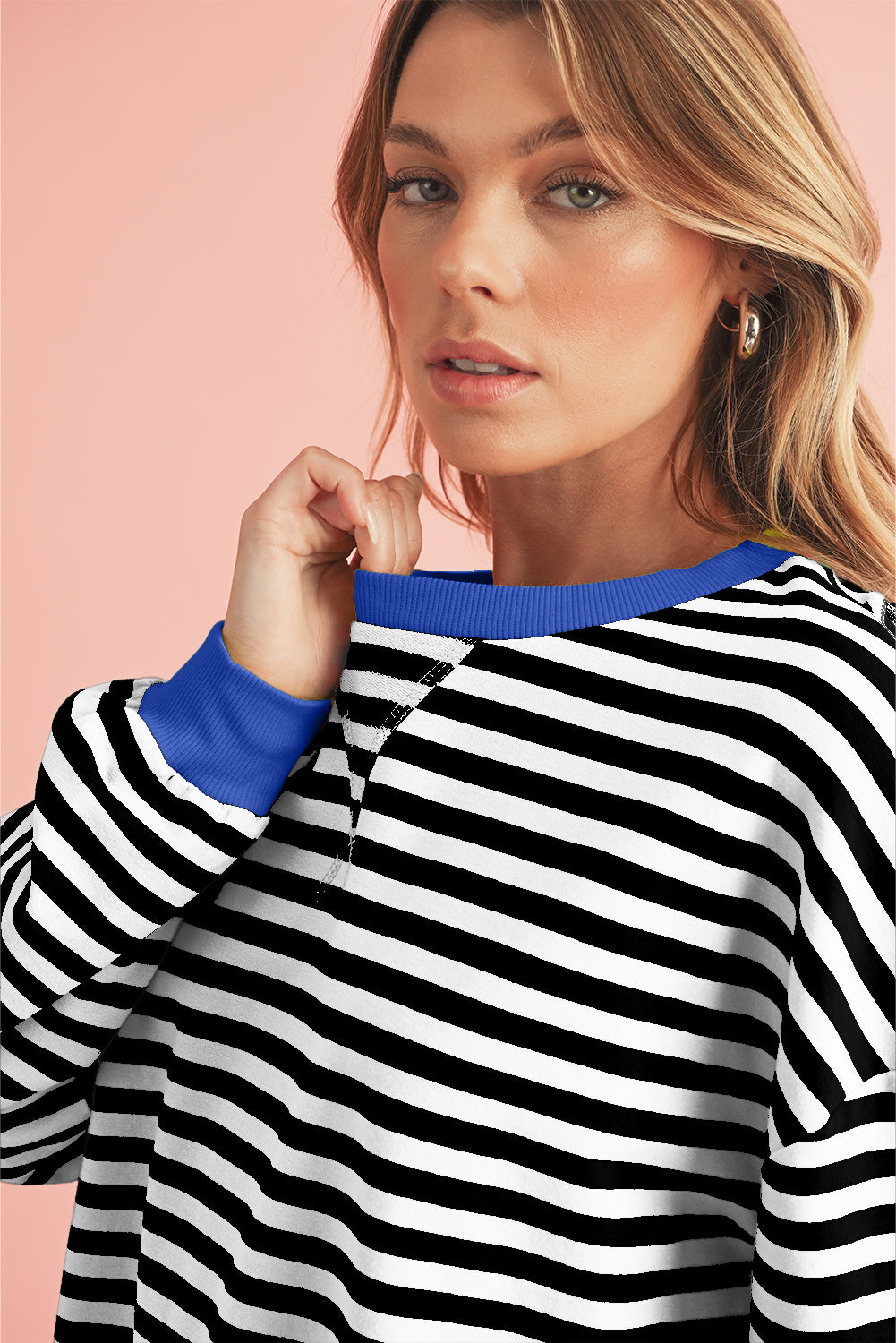 Woman wearing a black and white striped sweater with blue trim against a pink background