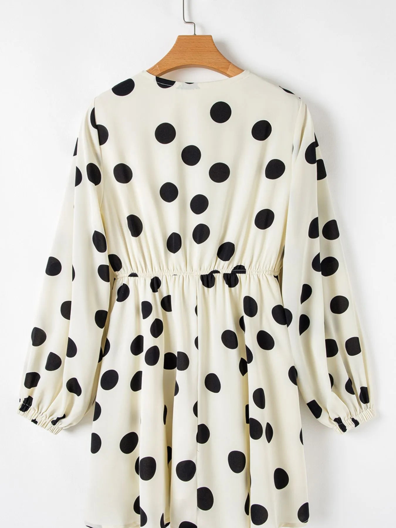 White dress with black polka dots on a wooden hanger against a white background