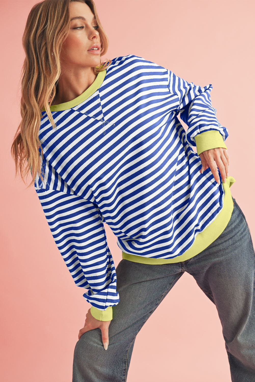Woman wearing a blue and white striped sweater with green trim on a pink background