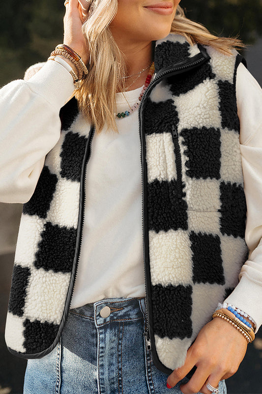 Person wearing a black and white checkered vest over a white shirt with denim jeans.