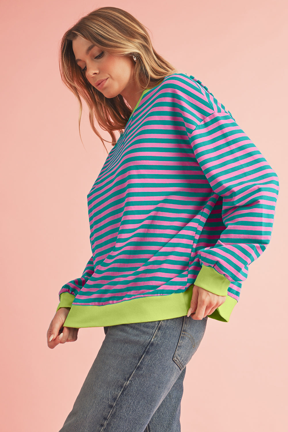 Woman wearing a striped sweater with green trim on a pink background