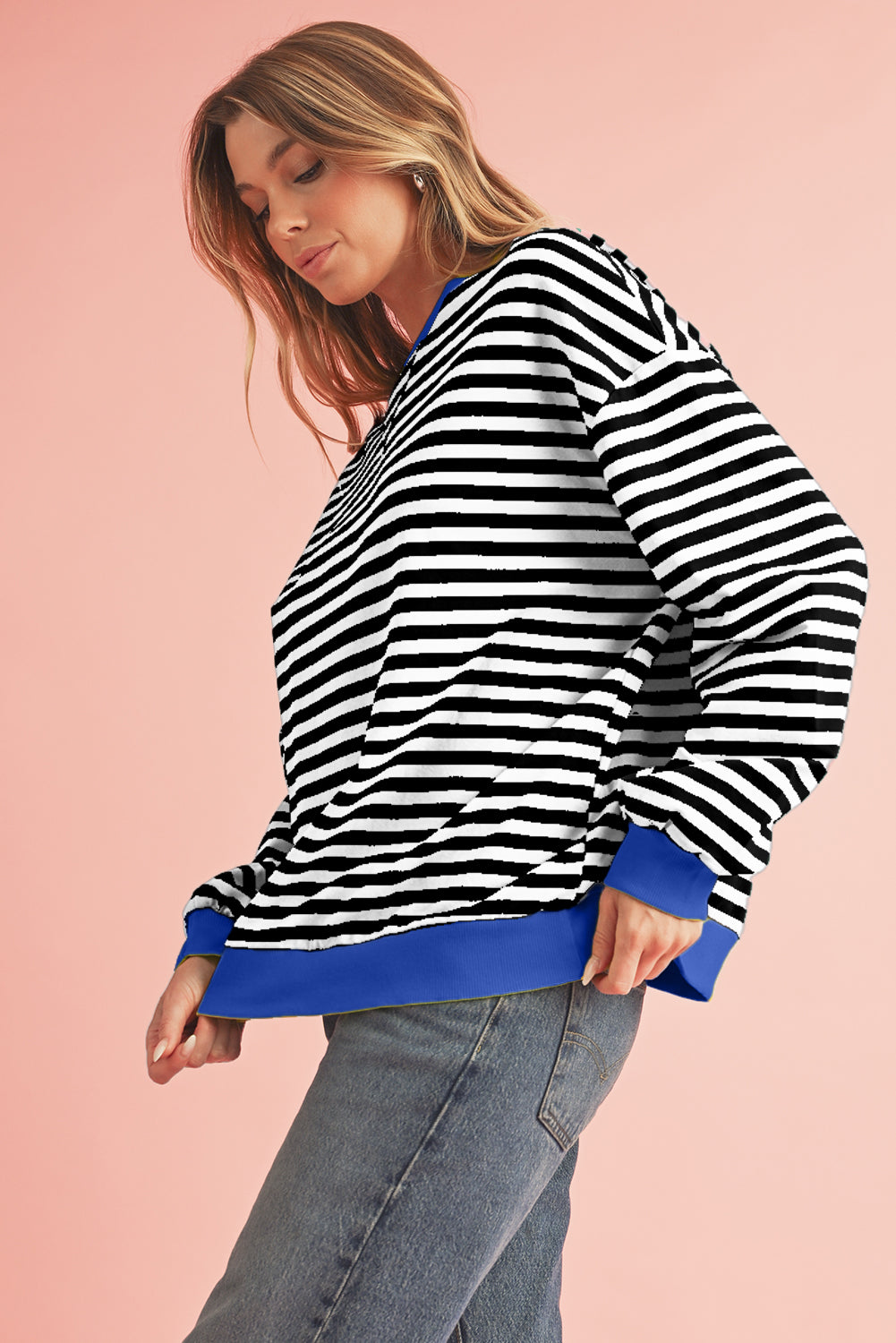 Woman wearing a black and white striped sweater with blue trim on a pink background