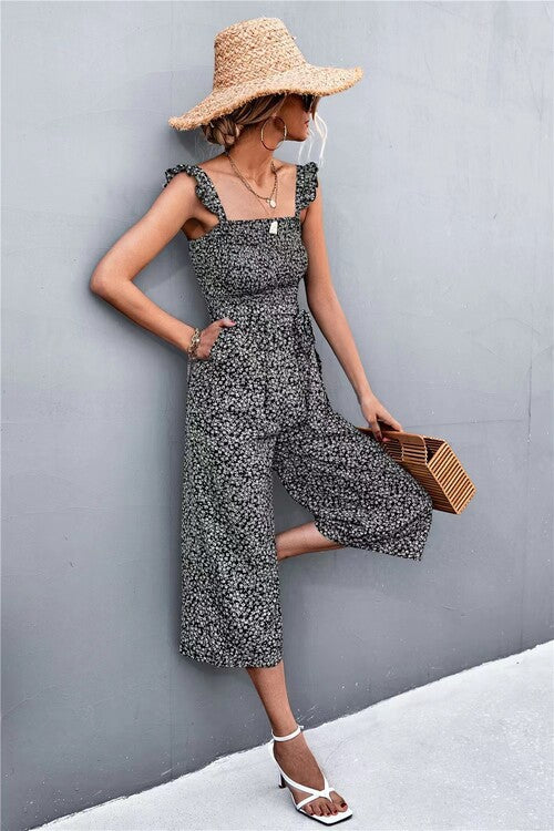 Woman in a floral dress and wide-brimmed hat against a gray wall