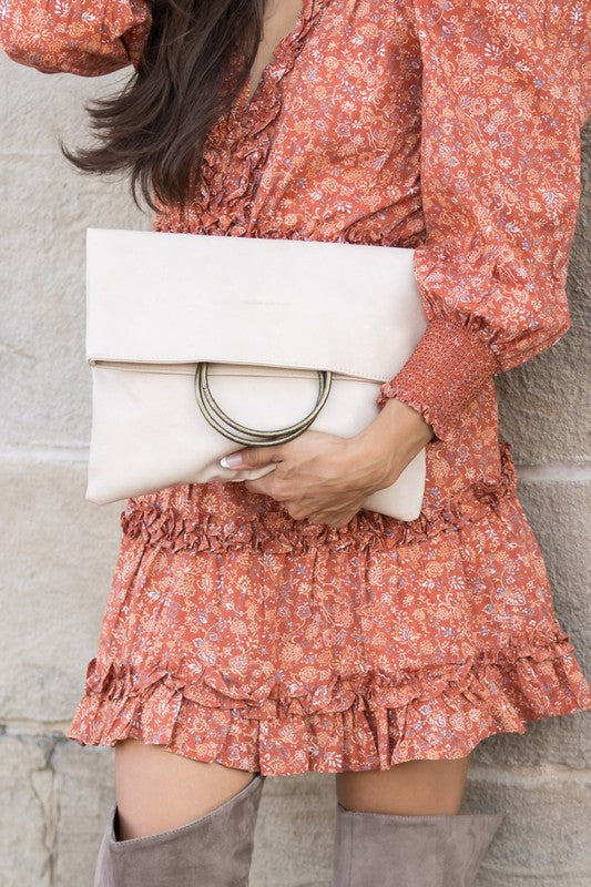 Person wearing a floral dress holding a white clutch against a stone wall.