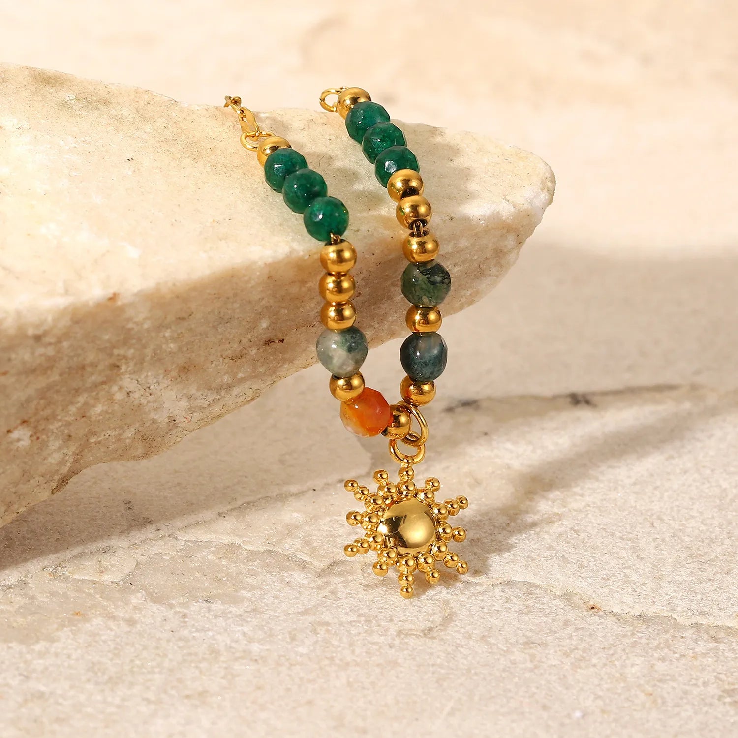 Beaded bracelet with gold sun charm on a stone surface